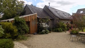 A rustic house with a gravel driveway, a wooden shed, and a garden with various plants and flowers. - Holiday home LES TIARELLES (Commana)