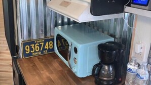Cozinha com torradeira azul, cafeteira e um relógio digital mostrando 10:35. Duas placas de automóvel à vista, uma de Nova Jersey e outra de Ohio.