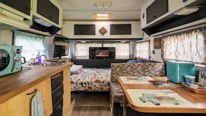 Interior compacto de uma RV com cozinha compacta, área de refeições, espaço para sentar e um pequeno centro de entretenimento.