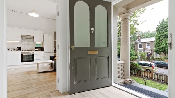 A modern kitchen with white cabinets and a built-in oven, a grey door with a number, and a view of a residential street. - Refined, Light 1 Bed Apt w Balcony in Brixton (London)