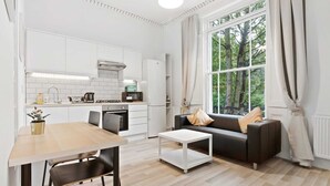 A modern kitchen with white cabinets, a dining table, and a sofa. - Refined, Light 1 Bed Apt w Balcony in Brixton (London)