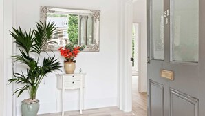 A hallway with a white door marked "51B", a white console table with a vase of red flowers, and a large mirror on the wall. - Refined, Light 1 Bed Apt w Balcony in Brixton (London)