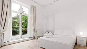 A bedroom with a large window, a bed, a bedside table, and a nightstand. - Refined, Light 1 Bed Apt w Balcony in Brixton (London)