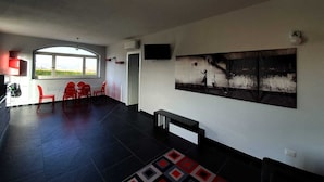 A spacious living area with a large window, a dining table with red chairs, a black sofa, and a wall-mounted TV. - Casa Appartamento Vacanza La Rondulina Suite (Tigliole)