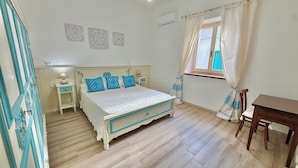 Un dormitorio con cama, mesitas de noche, ventana con cortinas y suelo de madera.