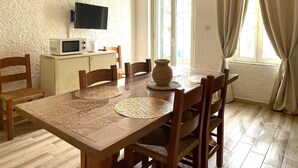 Un comedor con una mesa y sillas de madera, un televisor sobre un mueble bajo, y una ventana con cortinas.