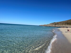 A beach with clear water, a sandy shore, and rocky cliffs in the background.