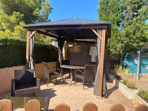 An outdoor patio with a covered seating area, a table, and chairs. - Casa Lisboa (Cala Mesquida)