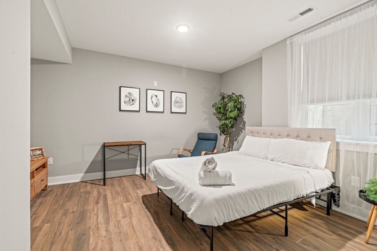 A modern bedroom with a bed, a desk, and a chair. There are three framed pictures on the wall.