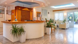Un área de recepción con mostrador de madera, zona de estar con sofá y sillones, y un gran ventanal con cortinas.