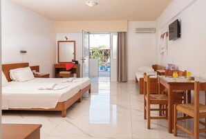 Habitación de hotel con cama, escritorio con silla, televisión y baño con espejo y retrete.