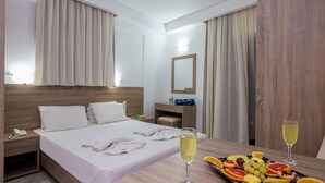 Una habitación de hotel con una cama bien hecha, una mesita de noche con una copa de champán y un plato de fruta sobre la mesa.