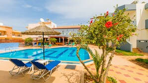 A swimming pool with lounge chairs and a thatched umbrella, surrounded by buildings and greenery. - Anthoula Village (Hersonissos)