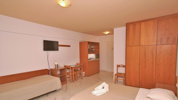 A hotel room with two single beds, a desk with a chair, a small kitchenette, and a wardrobe. - Anthoula Village (Hersonissos)
