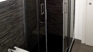 A modern bathroom with a glass-enclosed shower, dark tiled walls, and a white sink. - La Rondulina Classica (Tigliole)