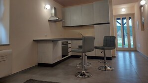A modern kitchen with two bar stools, a built-in oven, and a stainless steel range hood. - La Rondulina Classica (Tigliole)