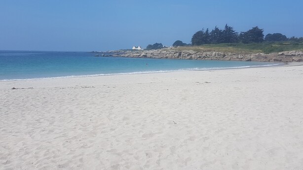 A beach with white sand, calm water, and a rocky outcrop with trees. - La Plage à Pied ! (Trégunc)
