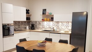 A modern kitchen with white cabinets, a black refrigerator, and a wooden dining table with chairs. - La Plage à Pied ! (Trégunc)