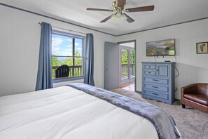 Quarto com uma cama grande, ventilador de teto, cômoda e vista para o exterior.