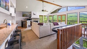 Een moderne keuken met een stenen openhaard, een zithoek met een witte bank en grote ramen met uitzicht op de groene omgeving.