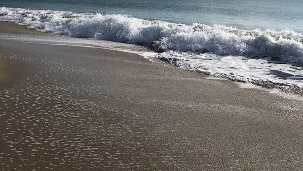 A beach with waves crashing onto the shore under a clear sky.