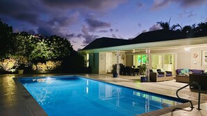 A swimming pool with a patio area, a dining table, and a sofa.