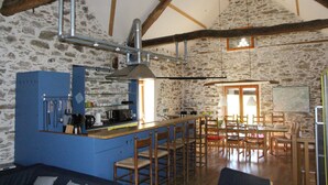 A rustic kitchen with a bar area, stone walls, wooden beams, and a dining area with wooden furniture.