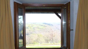 A room with a large window revealing a view of rolling hills and trees.