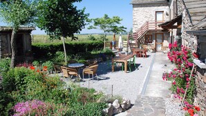 A rustic stone building with a wooden deck, outdoor seating, and a gravel pathway.