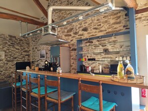 A bar area with stone walls, wooden chairs, and a counter with various items.