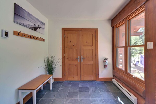 Un couloir avec une porte en bois, un banc, un porte-manteau et une fenêtre donnant sur l’extérieur.