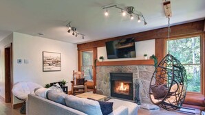 A cozy living room with a stone fireplace, a hanging chair, and a large sofa. - Family Lake Access Chalet w/ Spa (Lac-Supérieur)