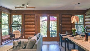 A cozy log cabin interior with a sofa, hanging chair, dining table, and large windows. - Family Lake Access Chalet w/ Spa (Lac-Supérieur)