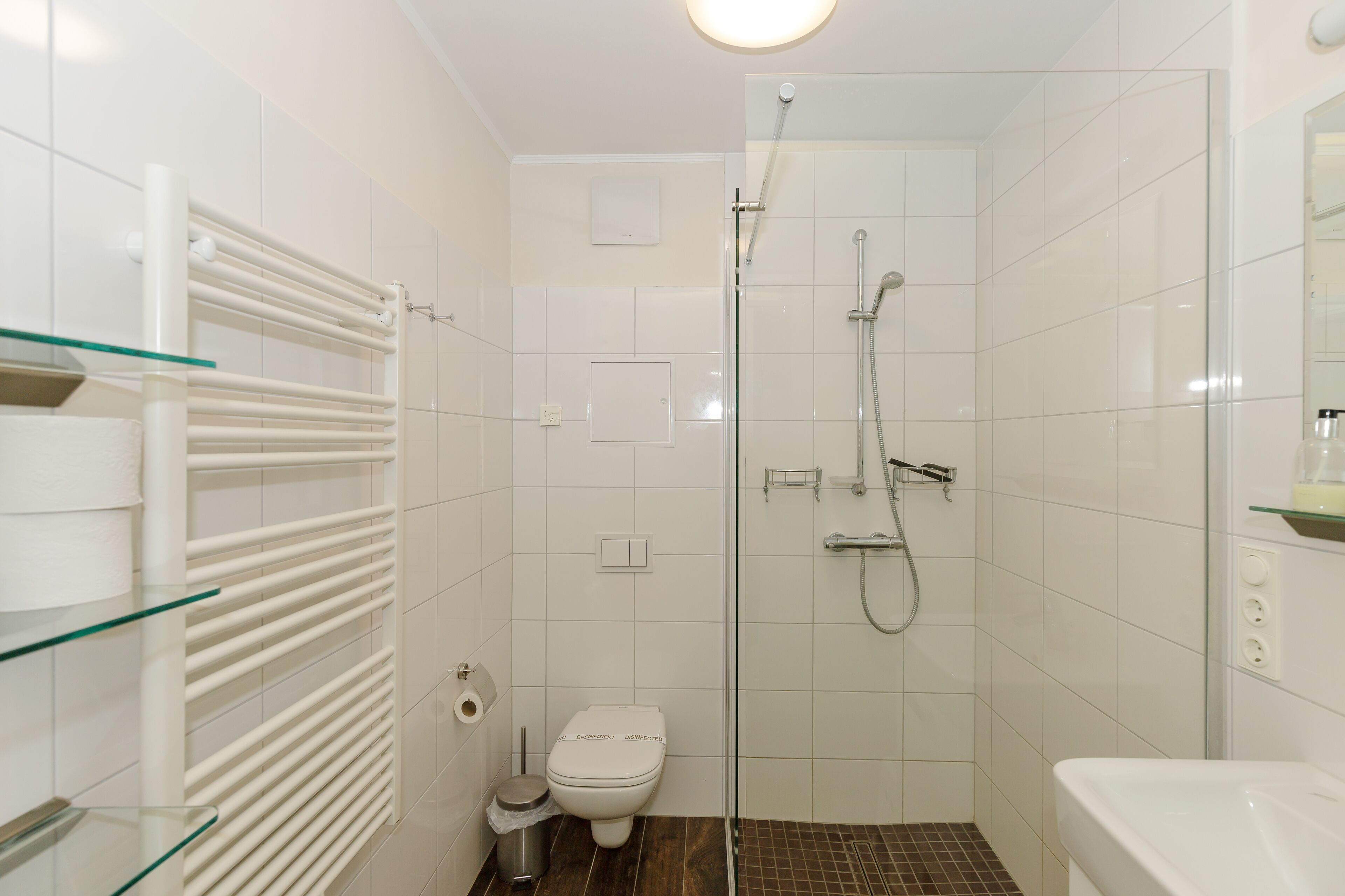A small, modern bathroom with a glass shower enclosure, a toilet, and a glass shelf with toiletries.