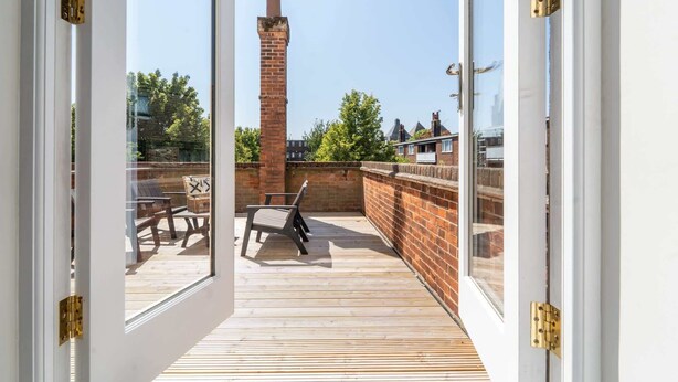 An open door leading to a balcony with a brick chimney, wooden flooring, and a table with chairs. - Luxury Apartment w/ Roof Terrace & Parking, Town Centre (Great Yarmouth)