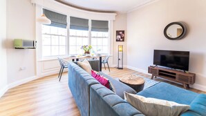 A living room with a sofa, TV, dining table, and large windows. - Luxury Apartment w/ Roof Terrace & Parking, Town Centre (Great Yarmouth)