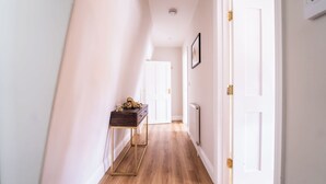 A hallway with a wooden floor, a dark wooden console table, and a white door at the end.
