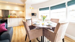 A modern kitchen with white cabinets, a dining table set for four, and a large window with curtains.