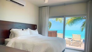 Ein Hotelzimmer mit einem großen Bett, einem Schreibtisch und Blick auf den Ozean durch eine Schiebetür.