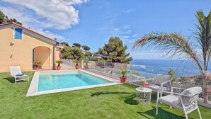 Ein Pool mit freiem Blick auf das Meer, eine Rasenfläche und eine Sitzgelegenheit mit Tisch und Stühlen.