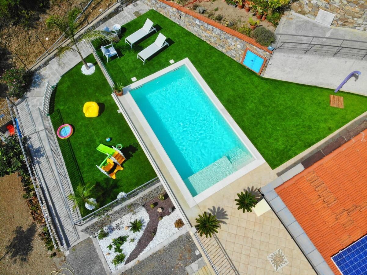 A rectangular swimming pool surrounded by a well-maintained lawn, a small play area with a slide, and a few lounge chairs.