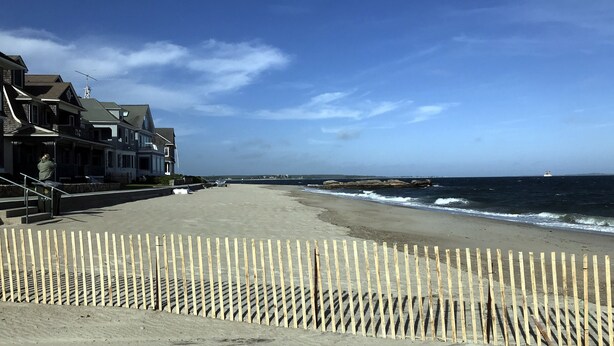 A beach with a wooden fence, houses in the background, and a boat in the water. - Great place for a large family reunion! (New London)