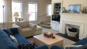 A living room with a beige sofa, blue armchairs, a coffee table, a fireplace, a TV, and a staircase leading to another room. - Great place for a large family reunion! (New London)
