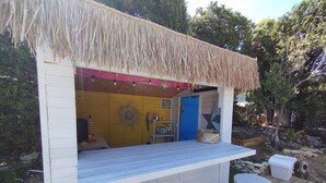 Un bar exterior de madera con techo de paja, una puerta azul y un interior rústico.