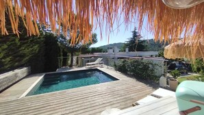 Una terraza de madera con piscina, sillas de descanso y una estructura de techo de paja.