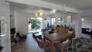 Amplia sala de estar con una mesa de comedor, sillas y un sofá. Un gran ventanal ofrece luz natural y vistas al exterior.