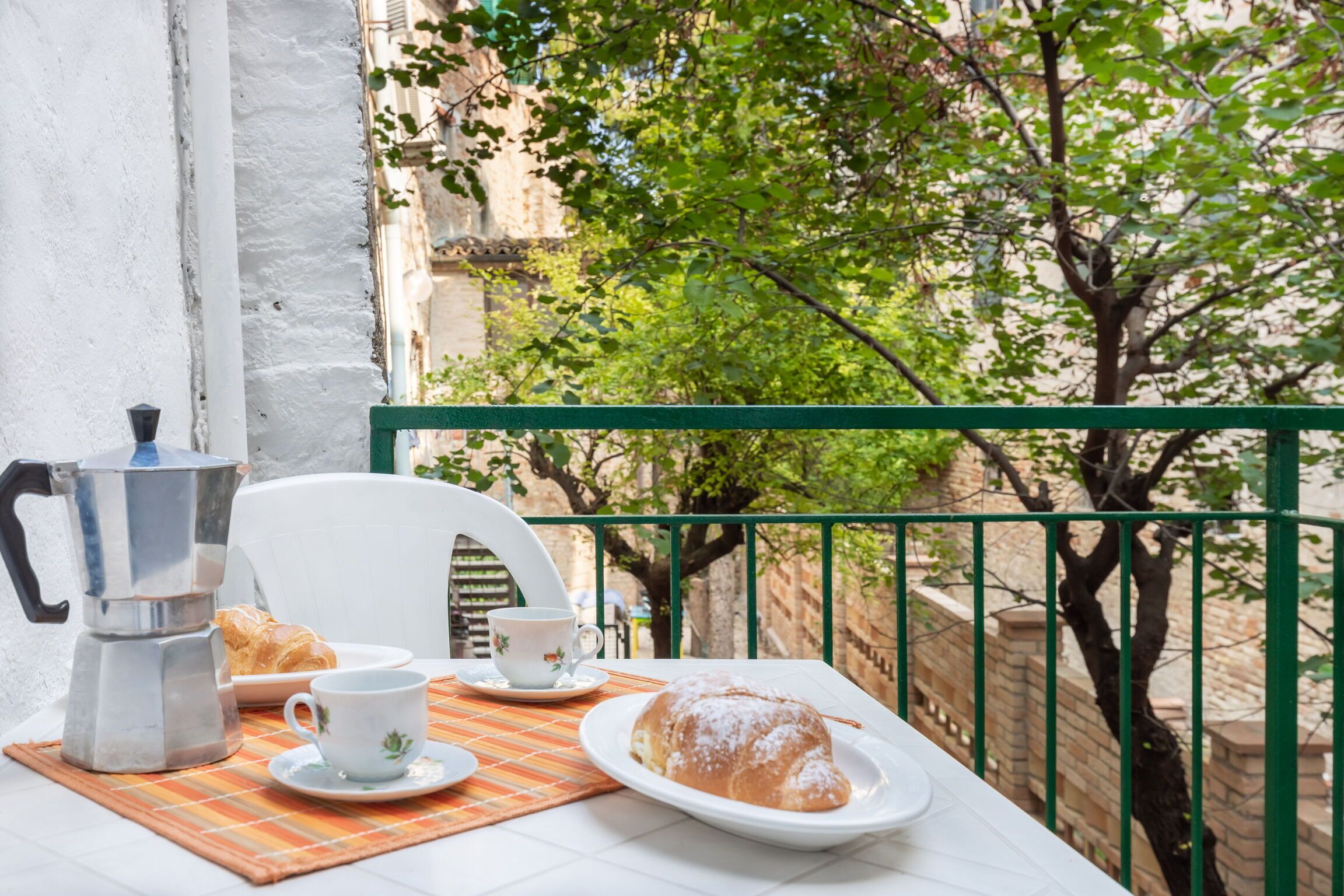 Un balcón con una mesa dispuesta para el desayuno, que incluye una cafetera, pasteles y una taza.