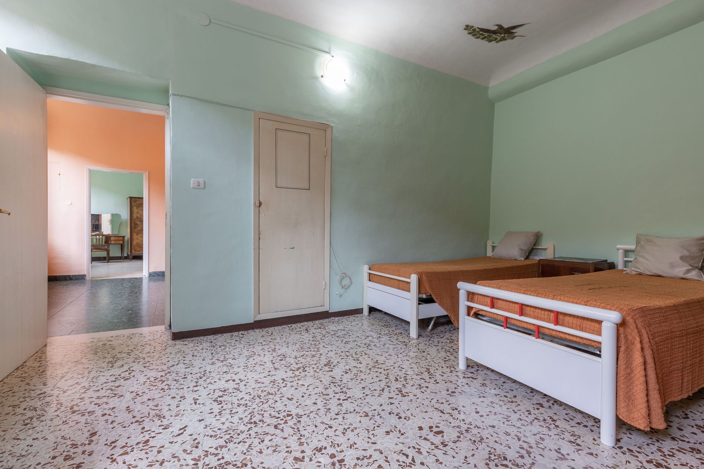 Een kamer met twee bedden, een deur en een betegelde vloer.