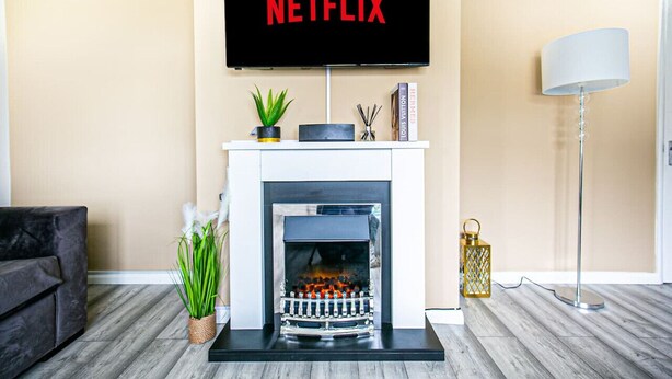 Una sala de estar con chimenea, un televisor sobre ella mostrando 