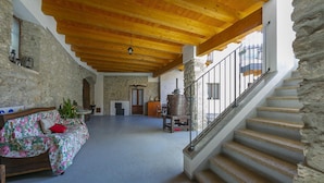 Una habitación con techo de madera, paredes de piedra, una escalera, un sofá con funda floral y una alfombra roja.